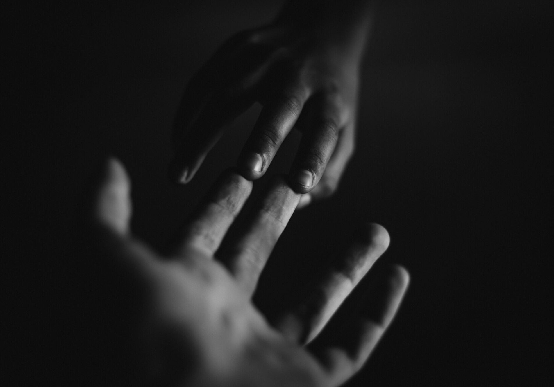 A touching monochrome image of two hands reaching towards each other, symbolizing connection.