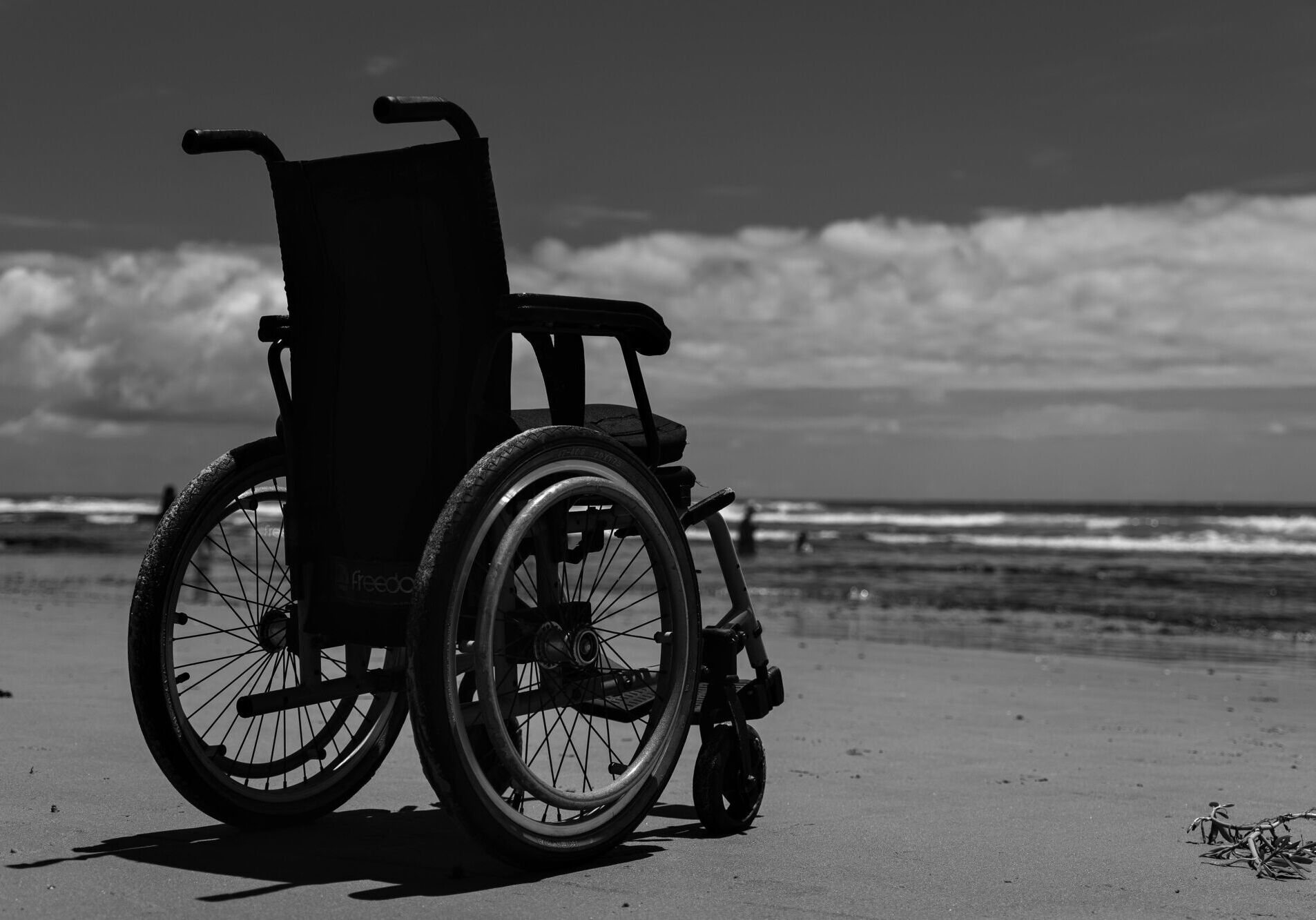 Black and white image of a wheelchair on a beach, symbolizing freedom and solitude.