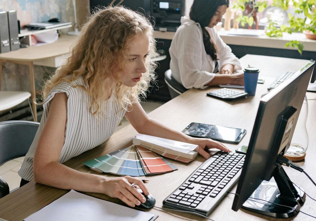 Two women focused on work at a desk, showcasing a vibrant and collaborative office environment.